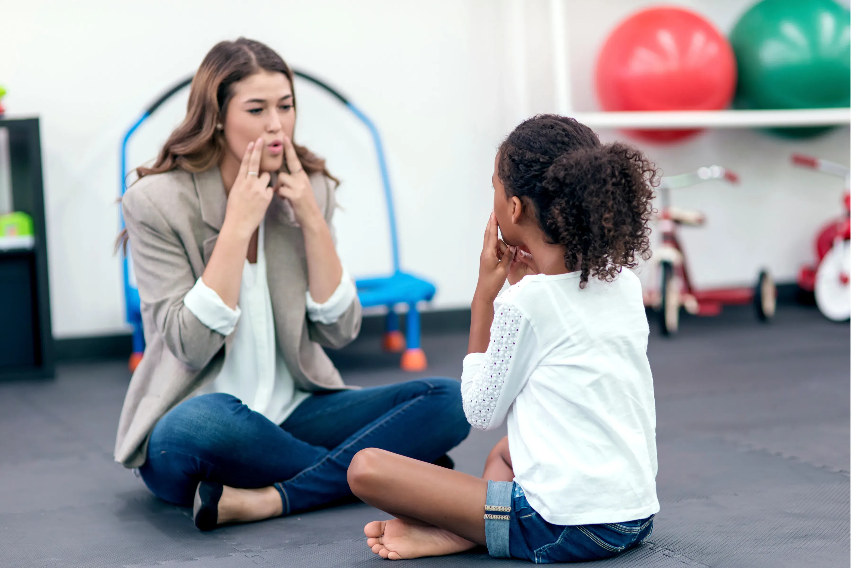 A clinician demonstrates mouth positioning to a young client.