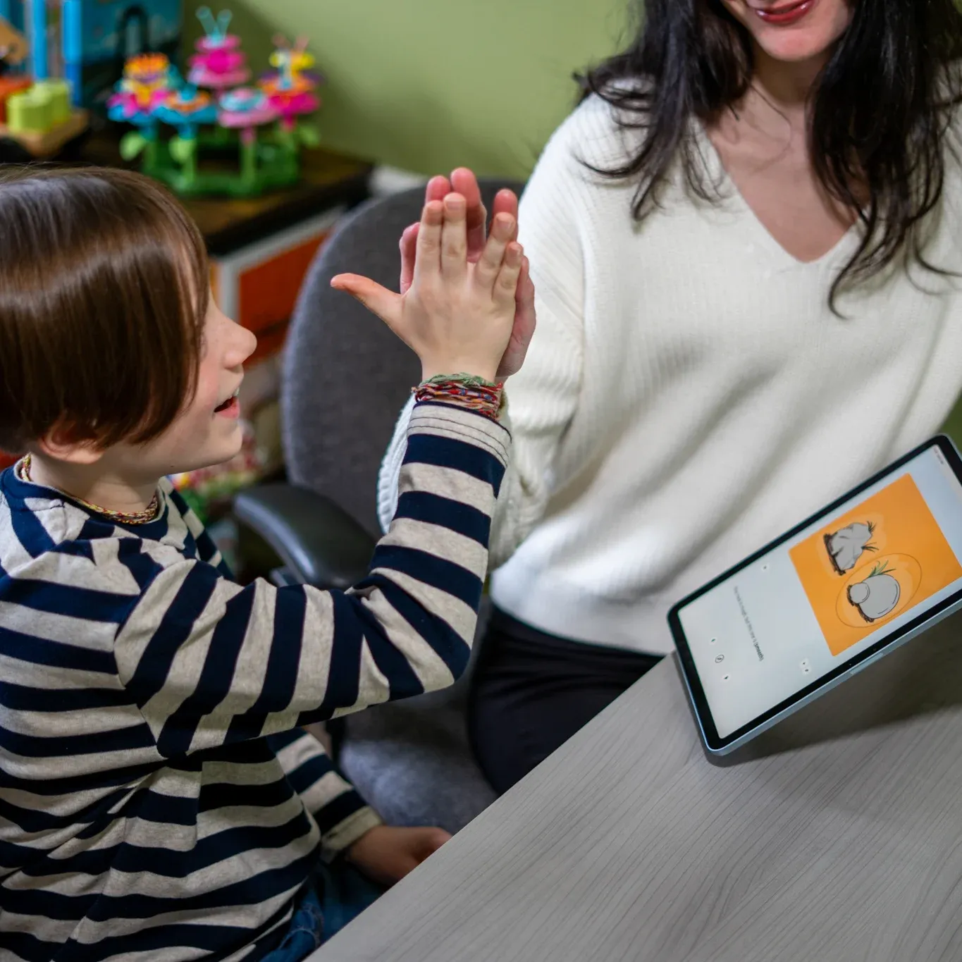 A speech professional and a young client high-five beside an iPad running SpeechCatcher.